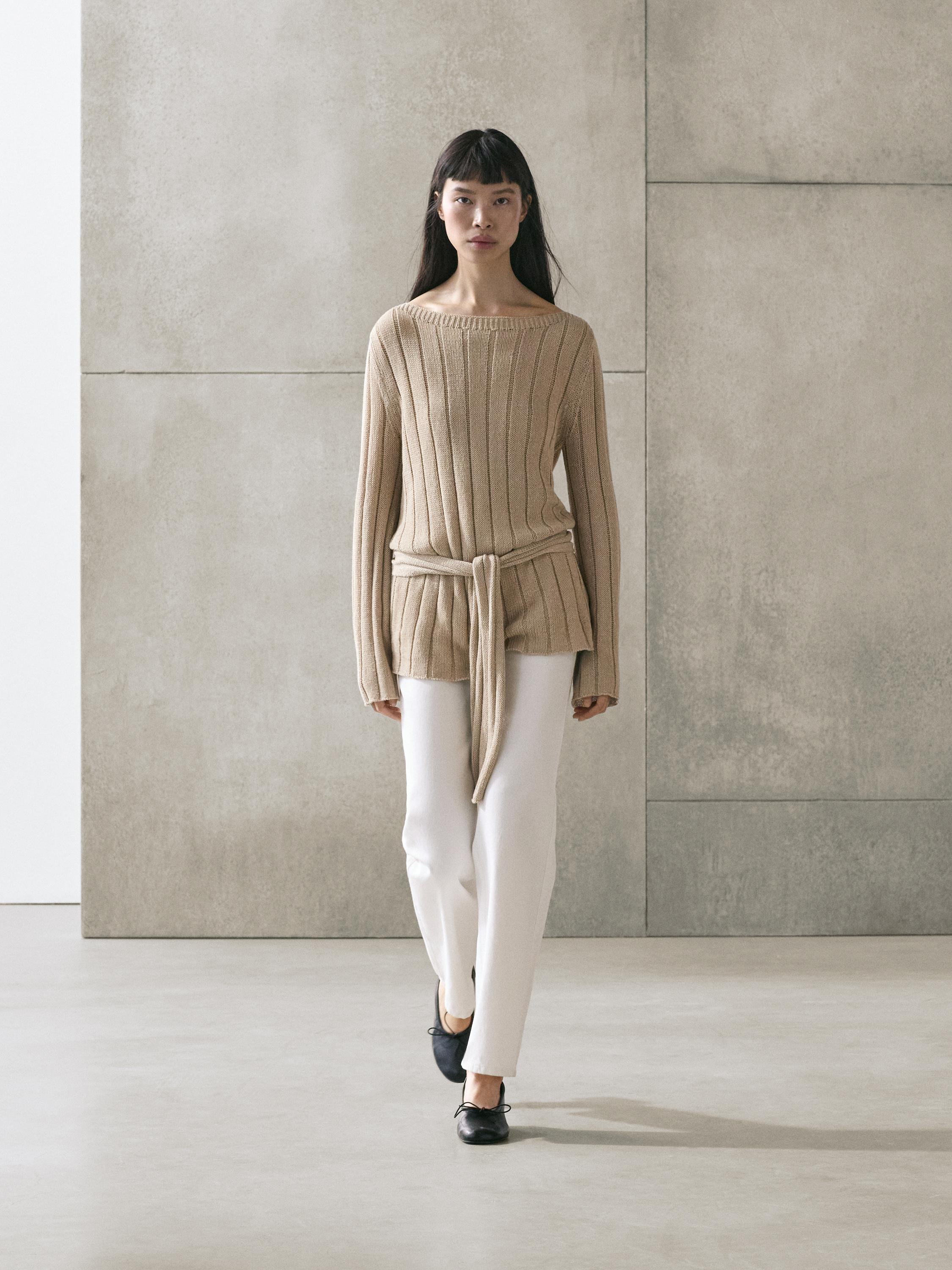 Beige knit boat neck sweater and belt set, paired with white pants and black shoes.