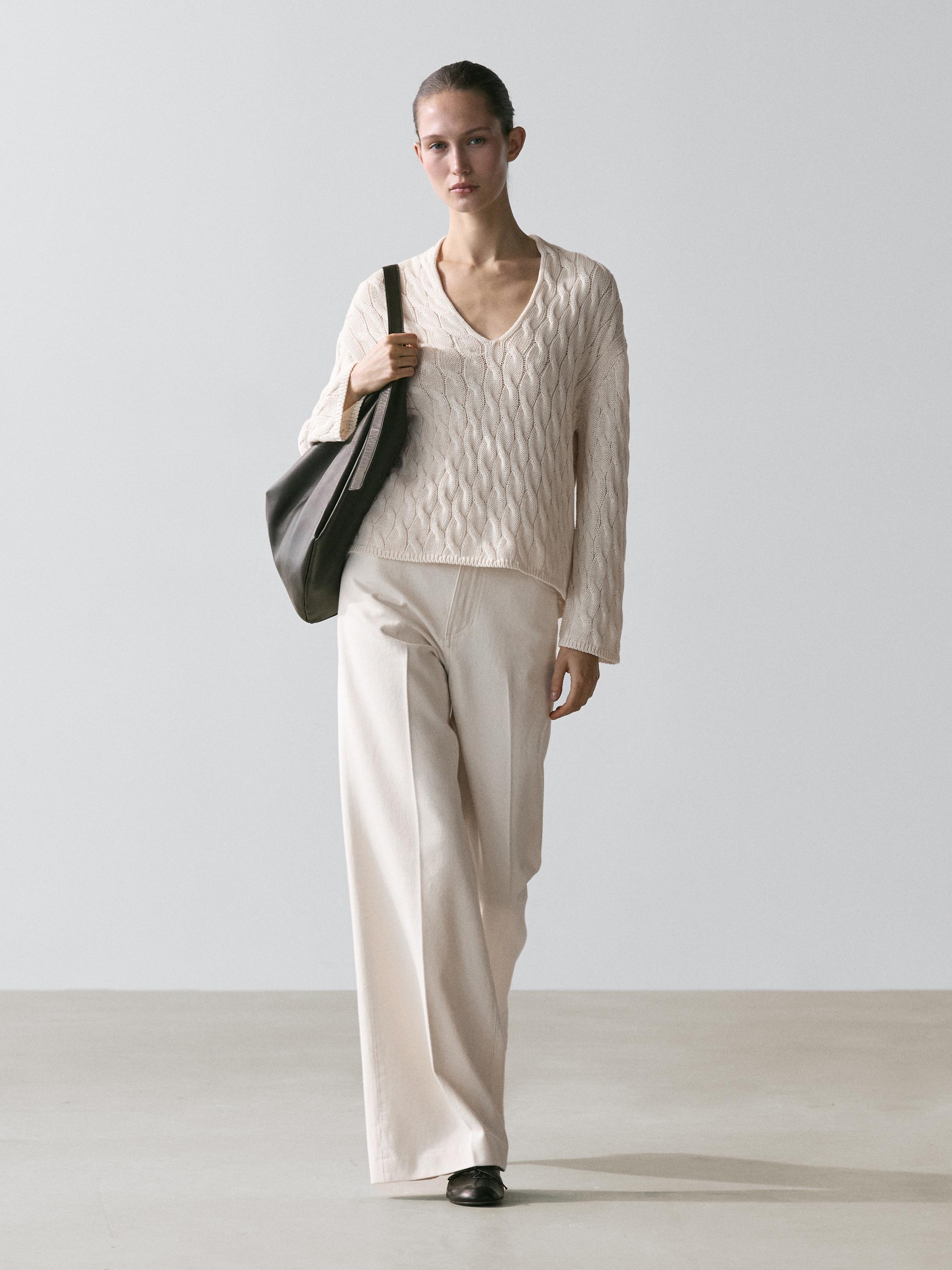 Комплект из джемпера цвета экрю с декоративными узлами и широких брюк в тон.
