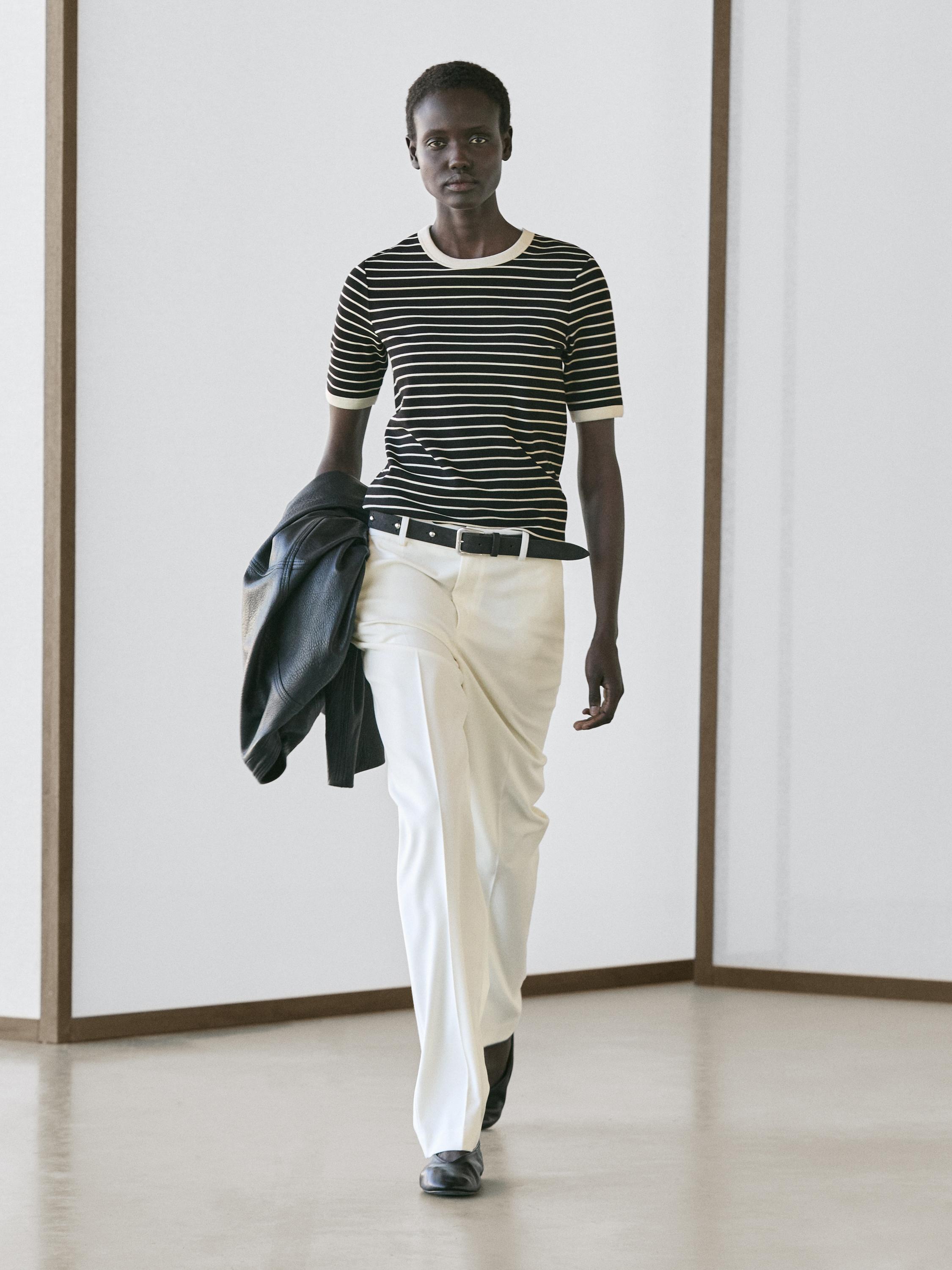 Set aus schwarzem T-Shirt mit weißen Streifen und gerader weißer Hose mit schwarzem Gürtel.