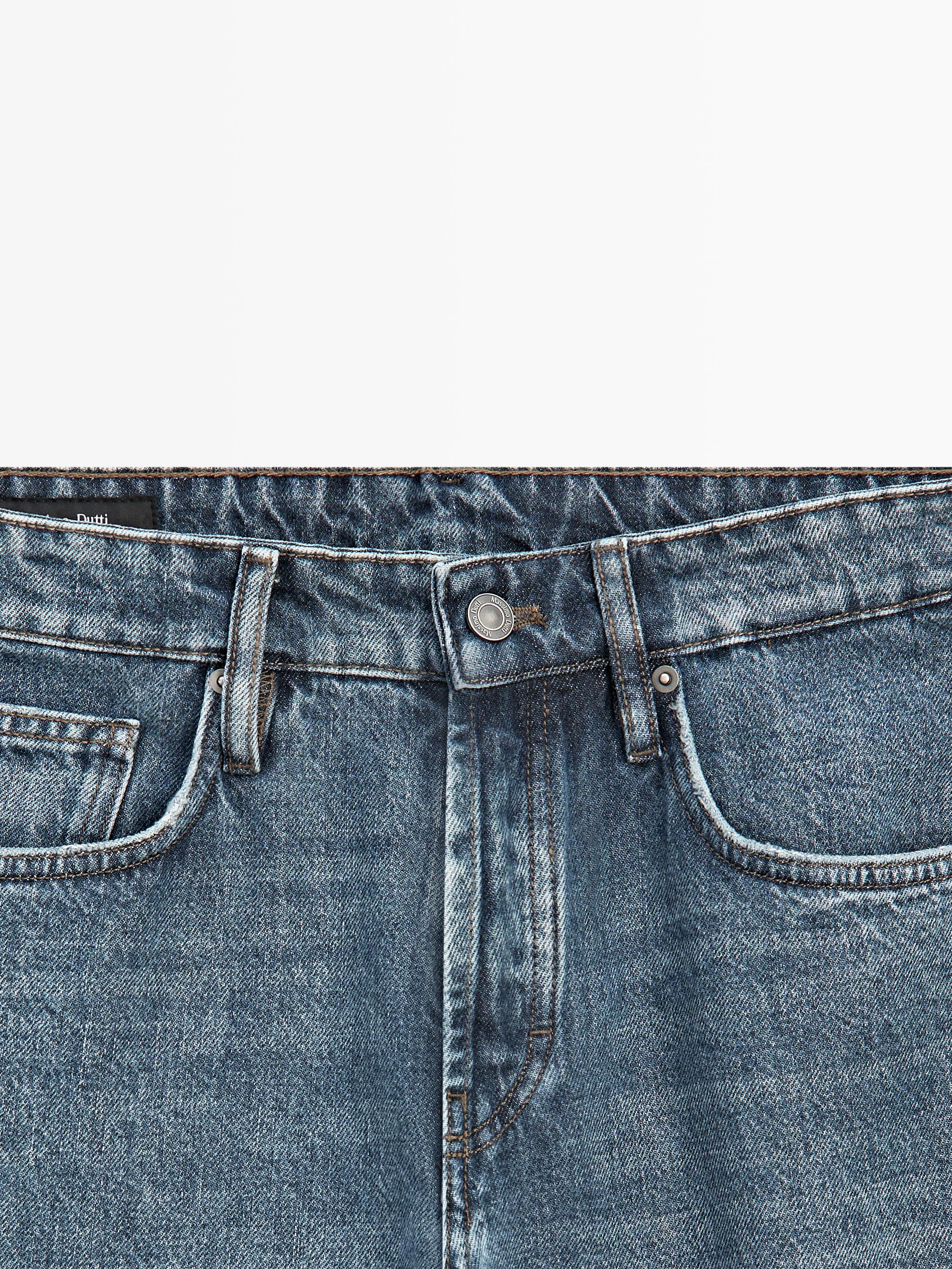 "Détail de la taille de jean bleu roi avec bouton métallique et poches avant visibles."