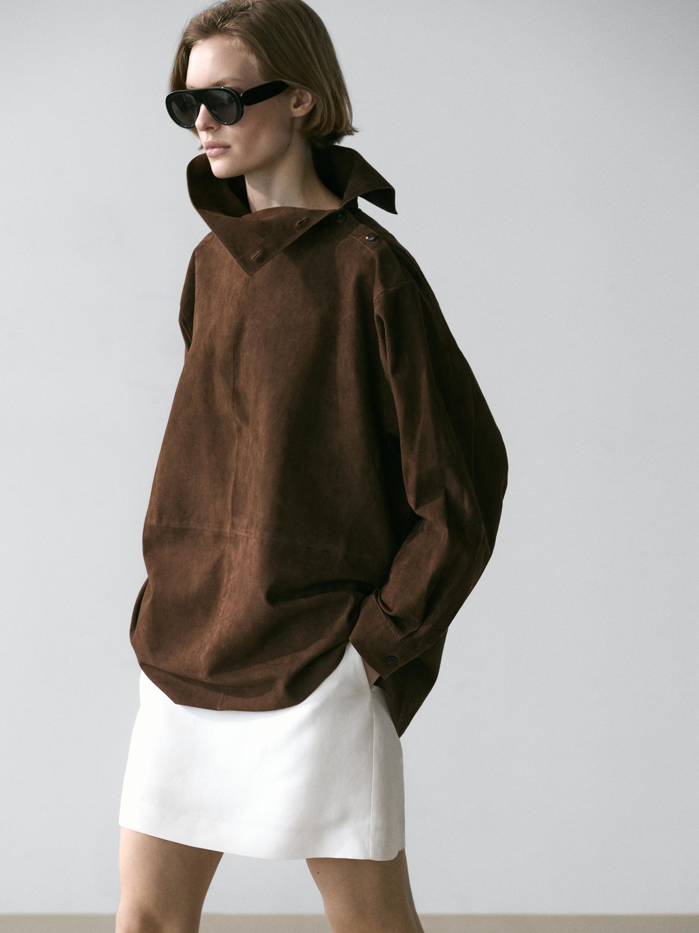 Conjunto de blusón marrón de cuello subido y falda blanca corta.