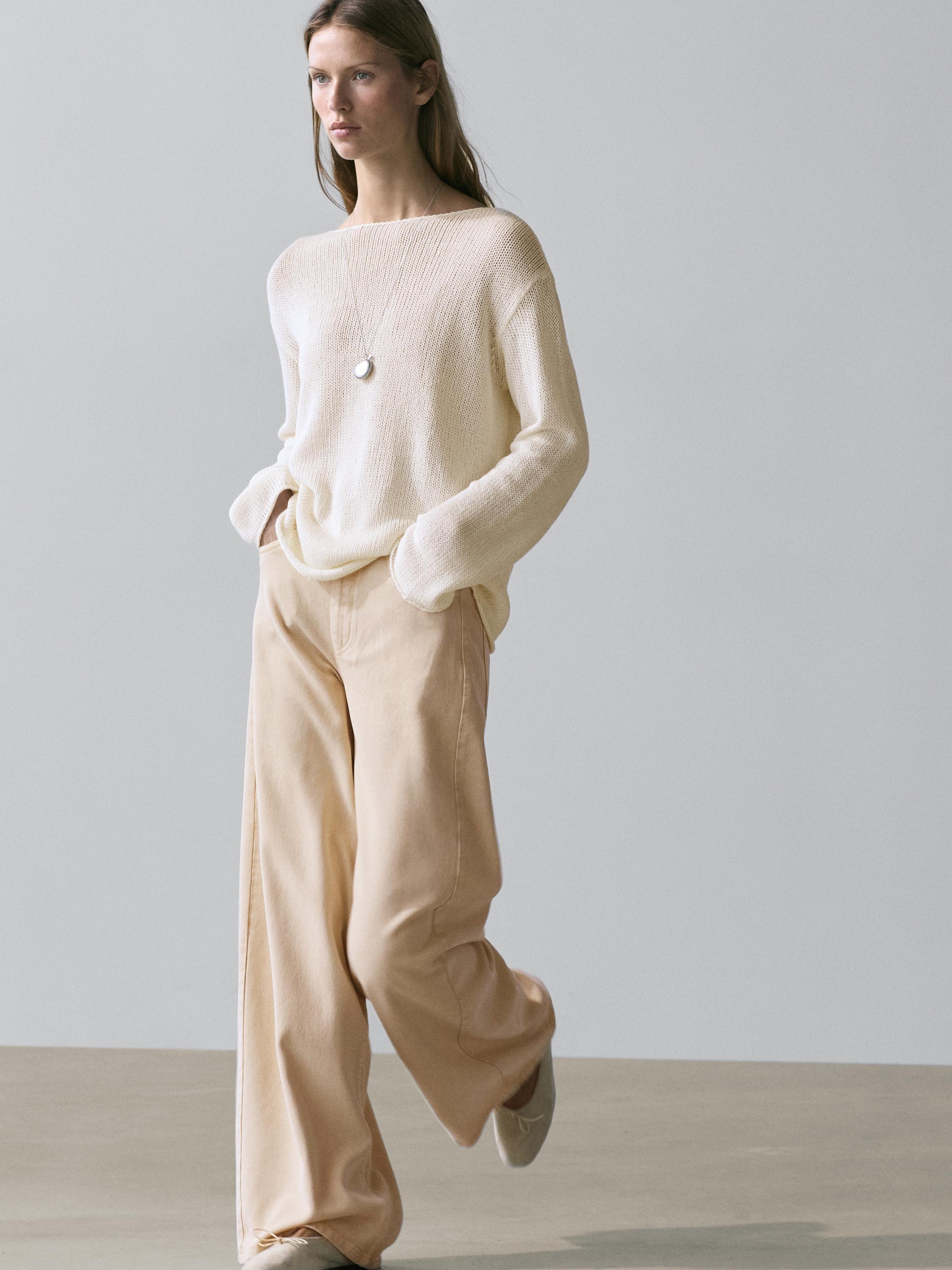 Conjunto de jersey crudo de punto calado con cuello redondo y pantalones beige de pierna ancha.