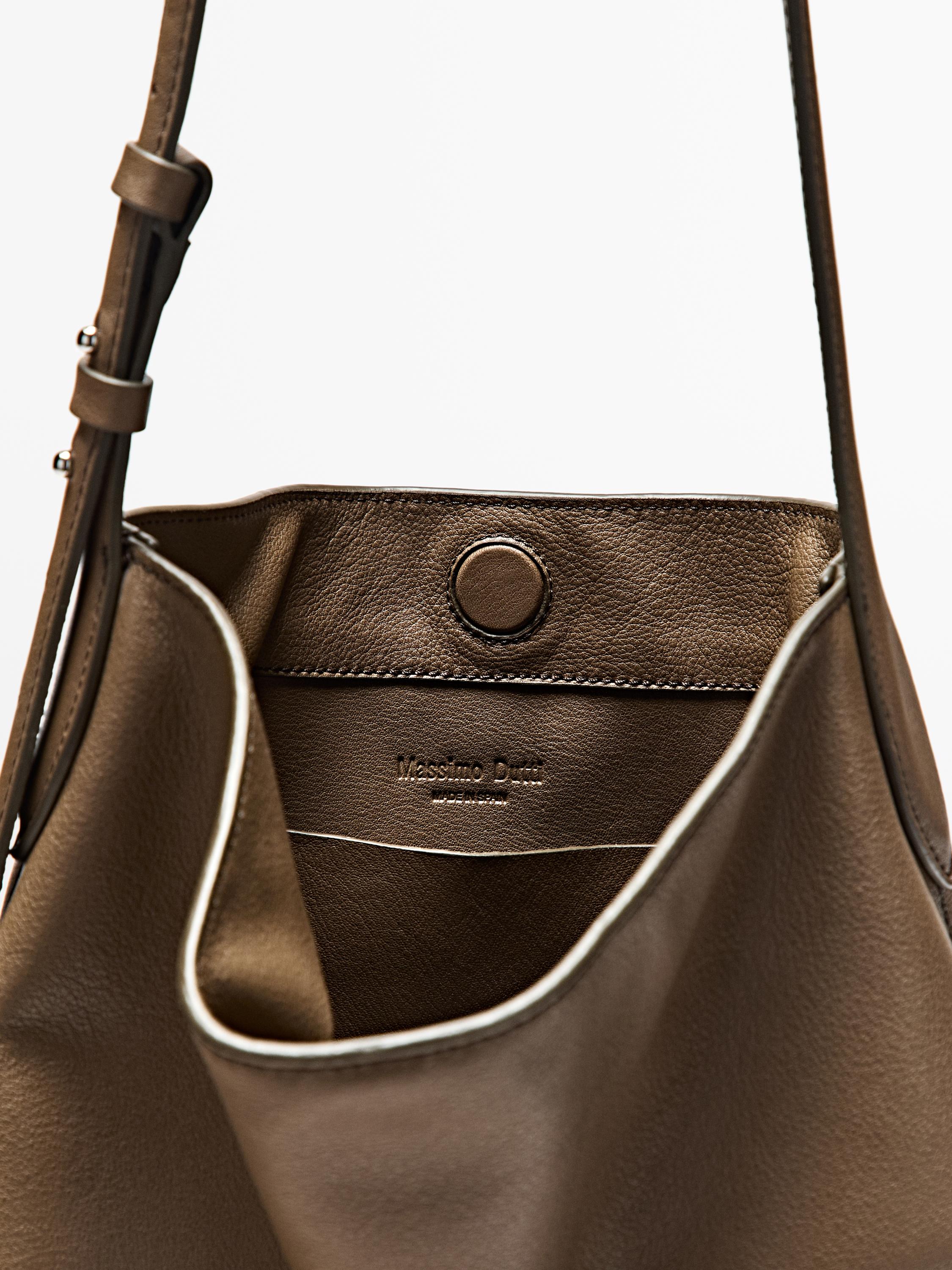 "Detail of a taupe brown handbag with magnetic closure and 'Massimo Dutti' text inside."