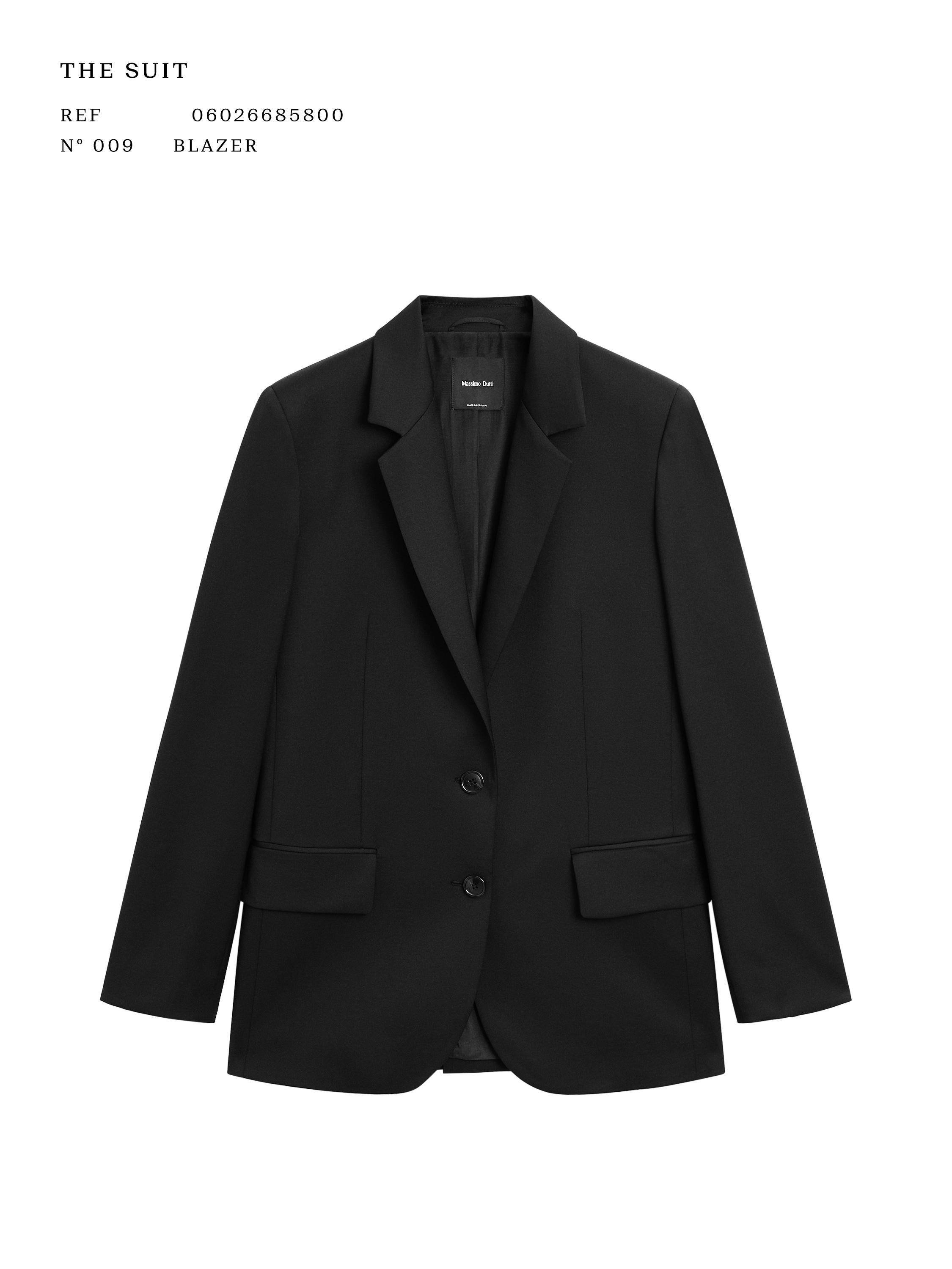 Vue de face d'un blazer noir avec revers classiques, fermeture à deux boutons et poches avant à rabat. Texte : "THE SUIT".
