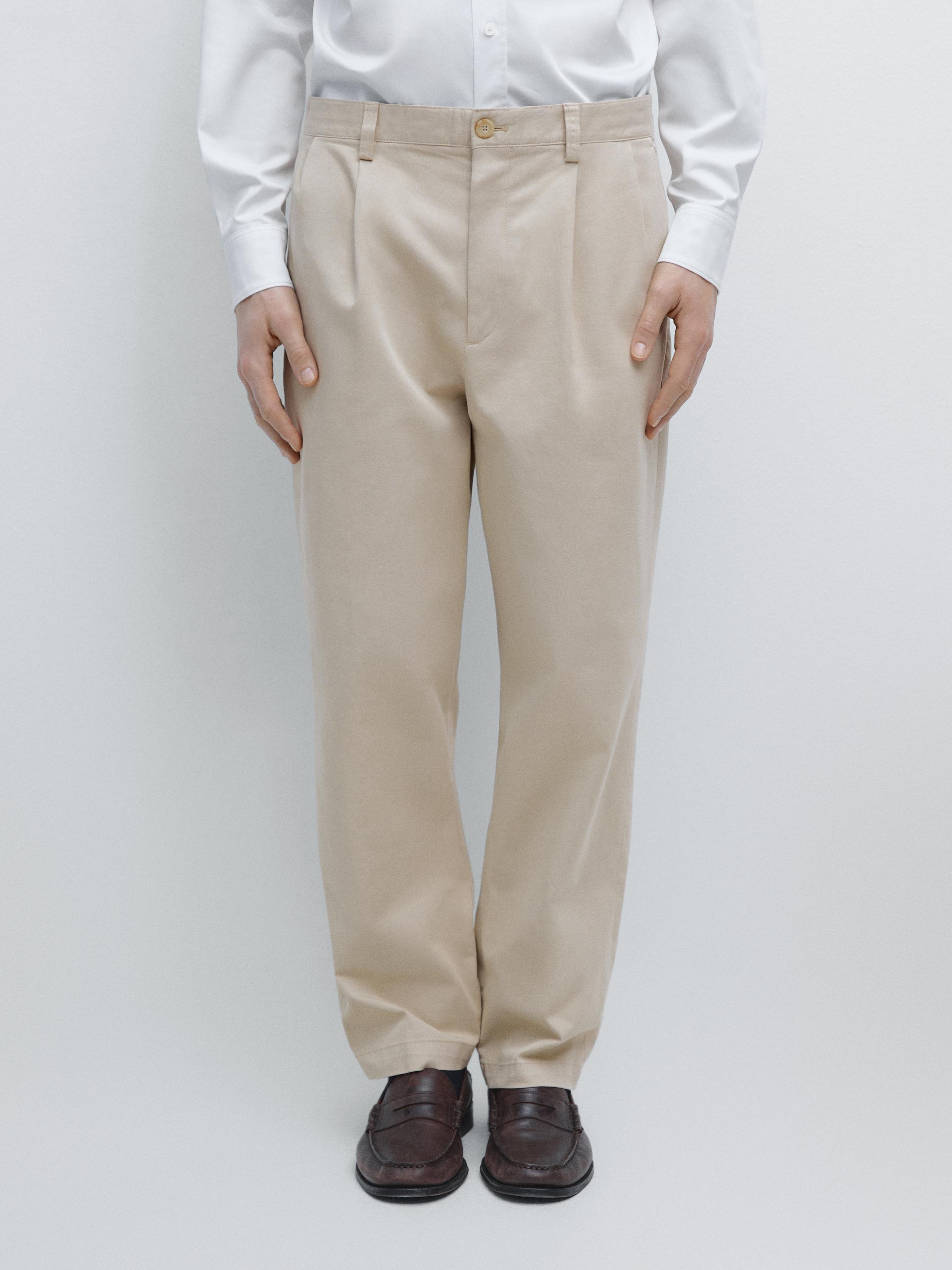 Beige pleated pants set with side pockets and button closure, paired with a white shirt.