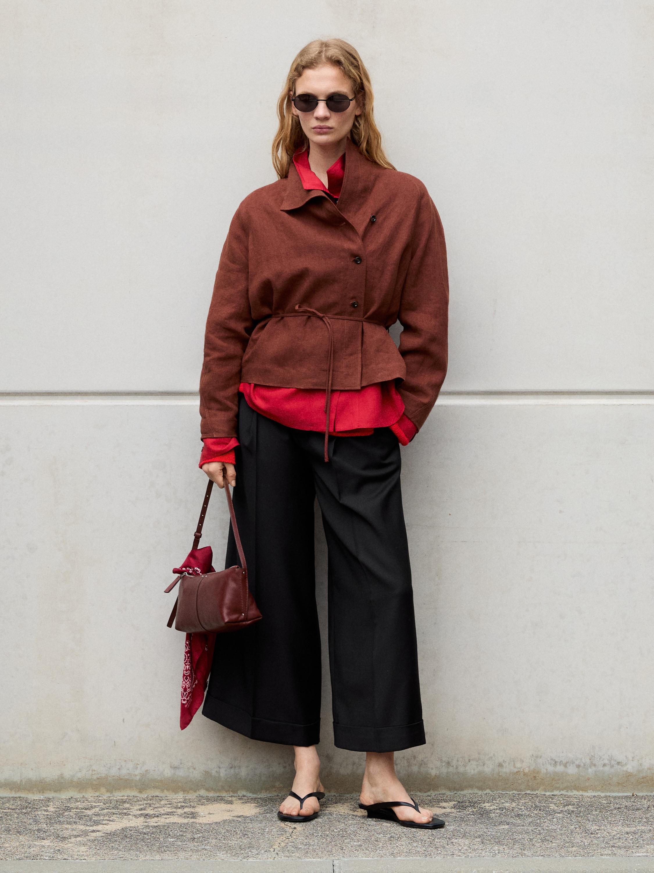 Kemerli kahverengi ceket takımı, kırmızı gömlek, geniş siyah pantolon ve siyah sandaletler. Kırmızı fularlı kahverengi çanta.