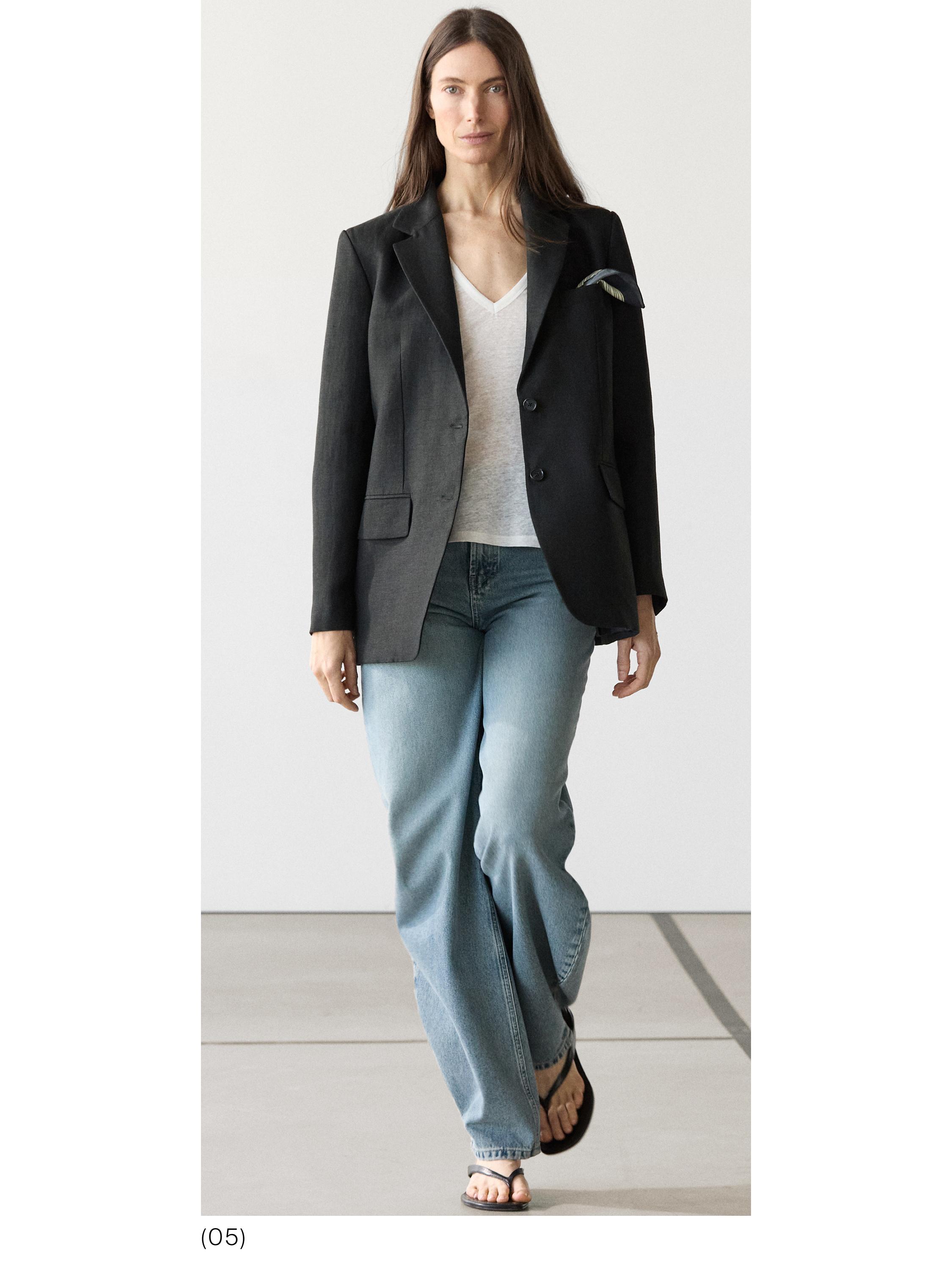 Conjunto de blazer negro con solapa, playera blanca de cuello en V, jeans azul claro y sandalias negras.